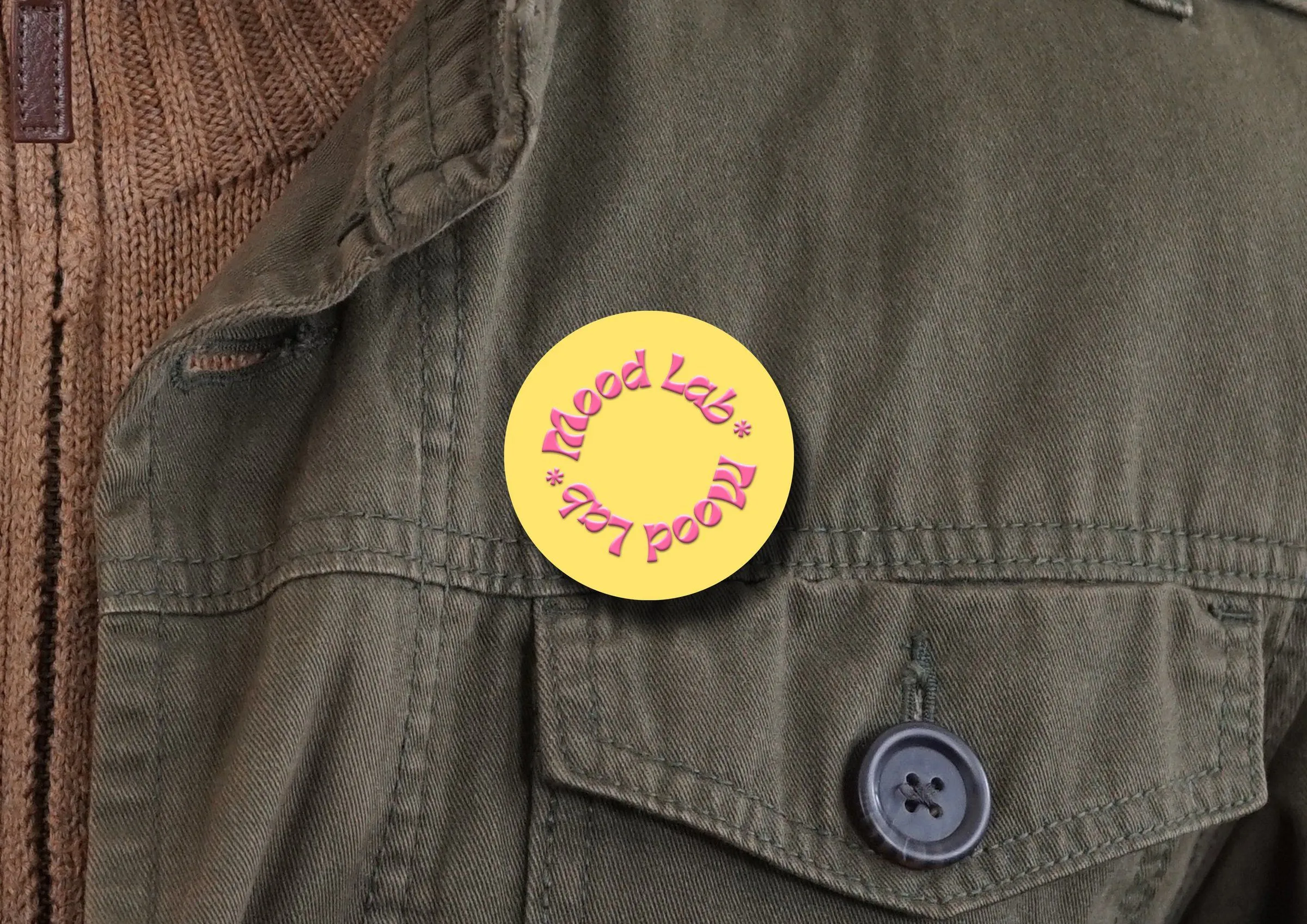 Pin amarillo de Mood Lab sobre una chamarra verde olivo